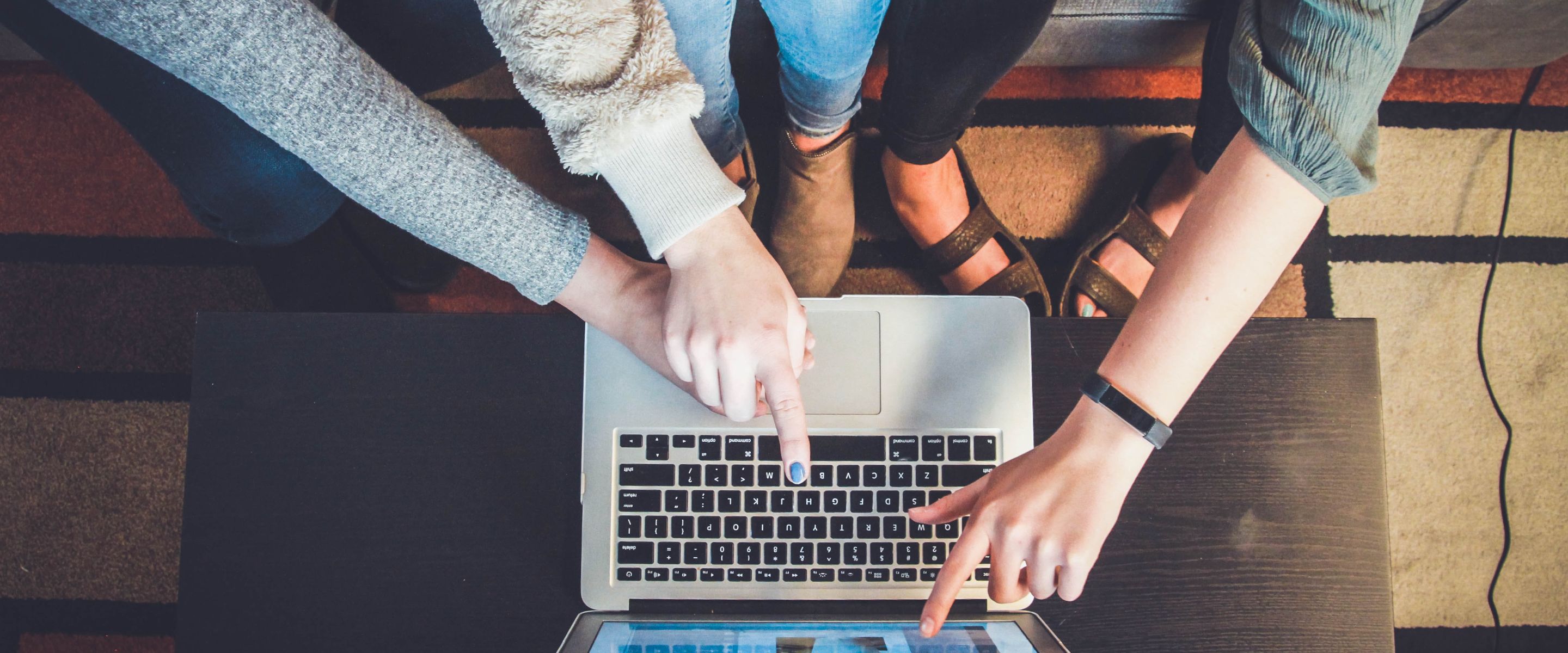Different hands pointing at a laptop screen