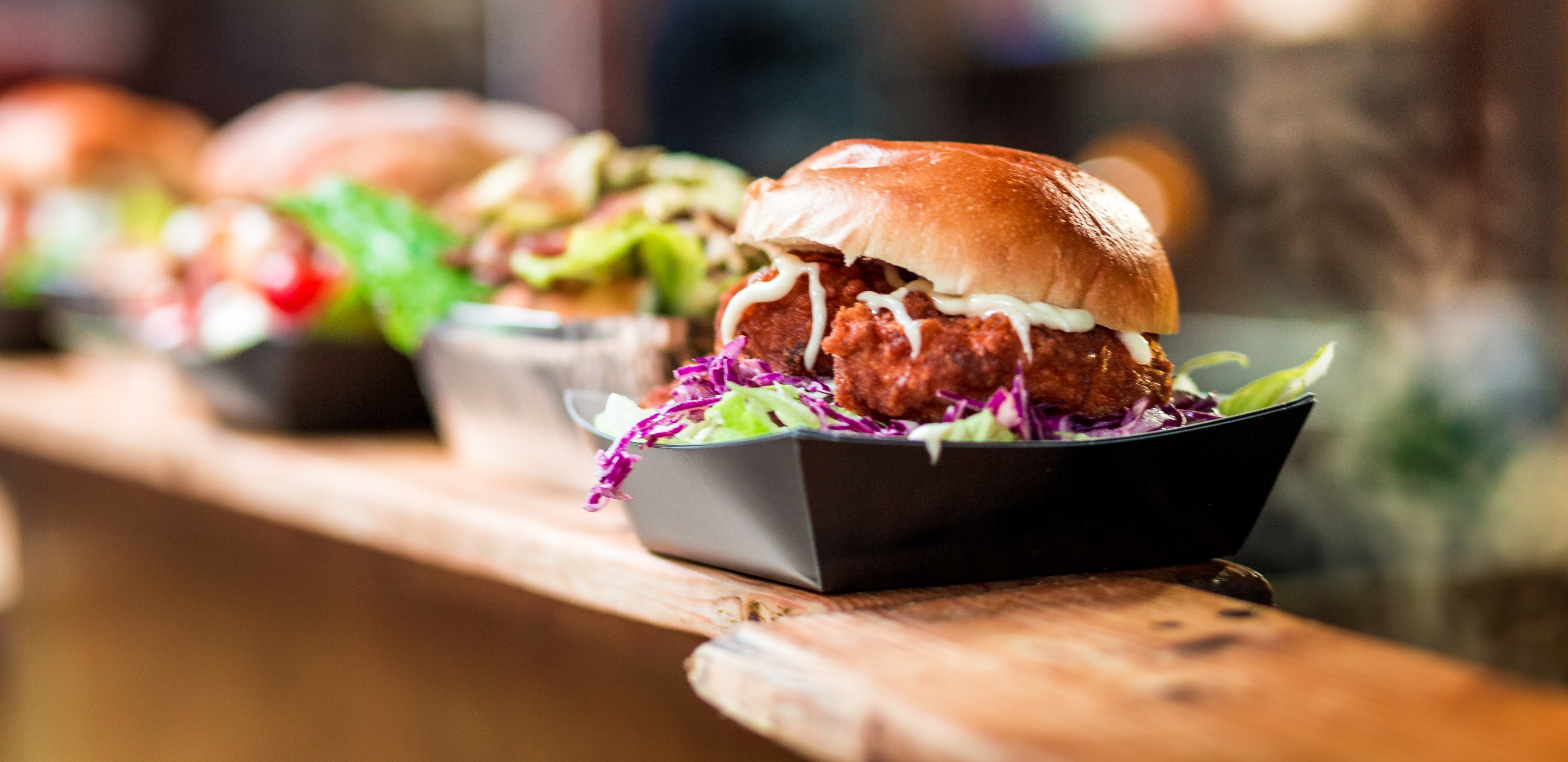 Gourmet burgers lined up on a wooden counter