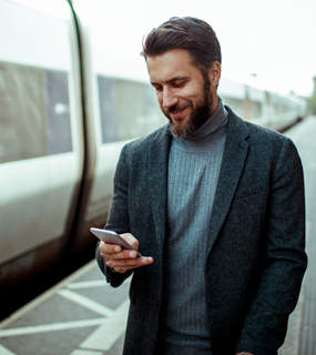 A man looking at a cellphone standing next to a train