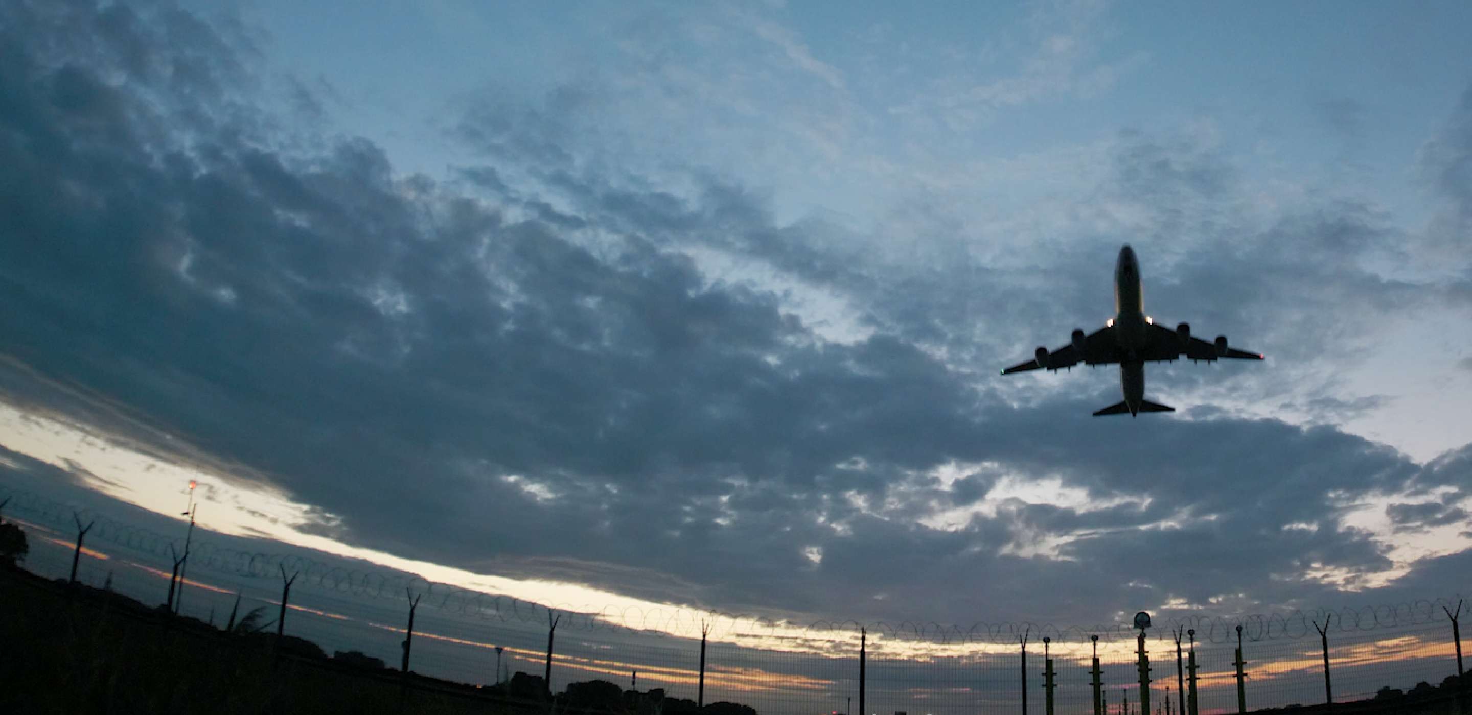 Silhouette of an airplane flying in front of cloudy sky