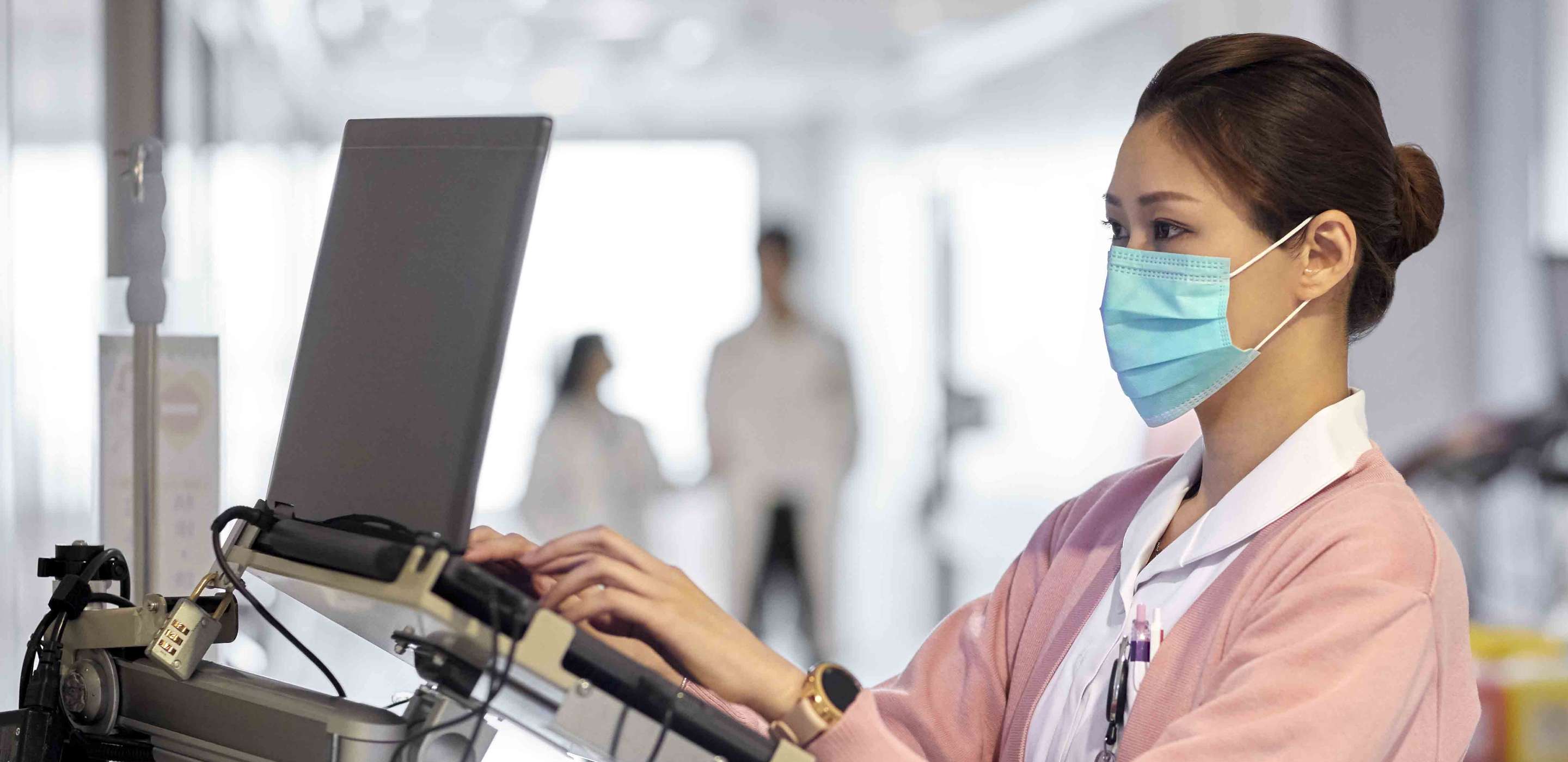 A woman with a mast typing while standing
