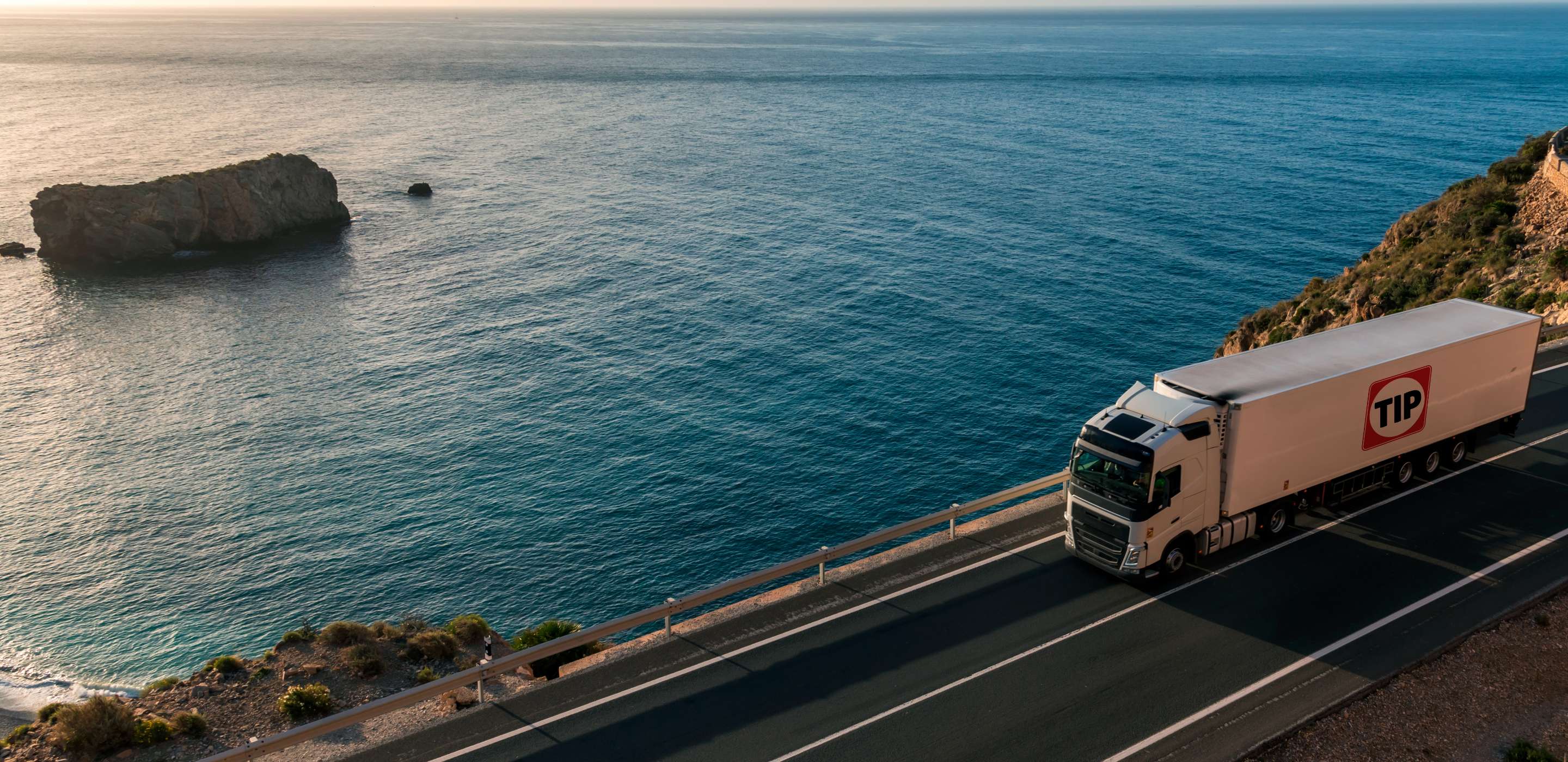 A big truck on a hill road next to water