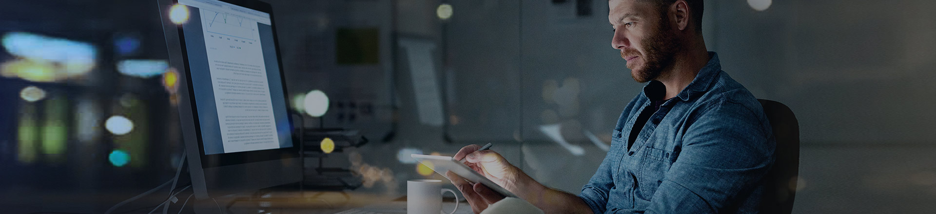 Man with a mobile device sitting at a computer screen